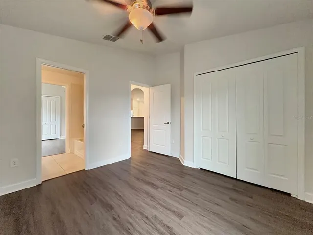 a view of an empty room with wooden floor and a ceiling fan