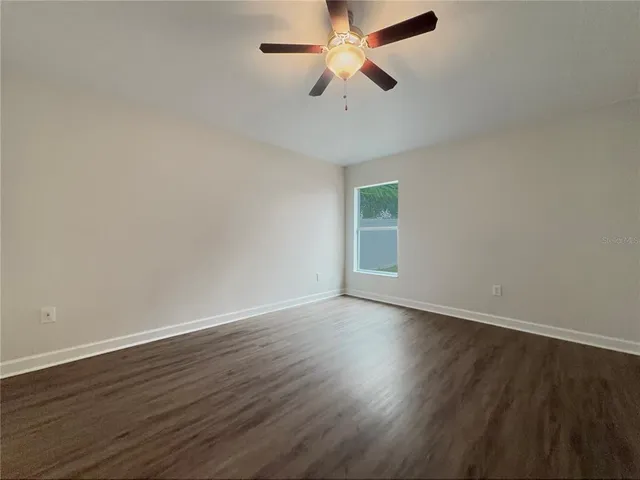 a view of an empty room with wooden floor and a ceiling fan