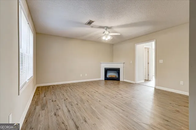 an empty room with wooden floor fan and windows