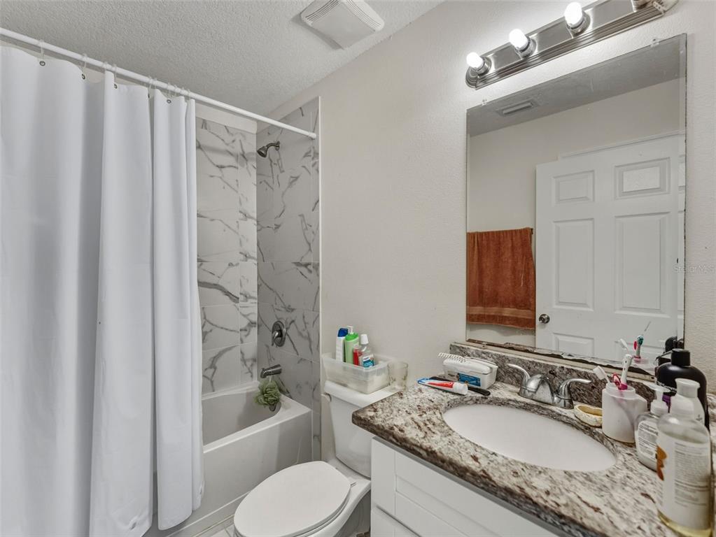 5104 Timberlan Street Tampa, FL 33624 - Photo 19 of 27 a bathroom with a granite countertop sink toilet a mirror a bathtub and shower