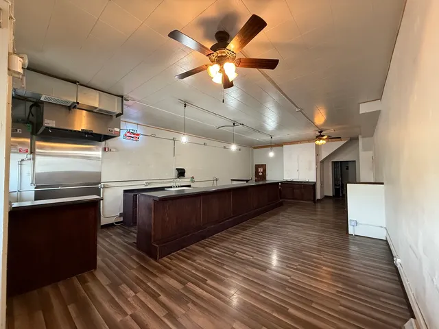 a living room with stainless steel appliances kitchen island granite countertop a refrigerator a stove and a wooden floors