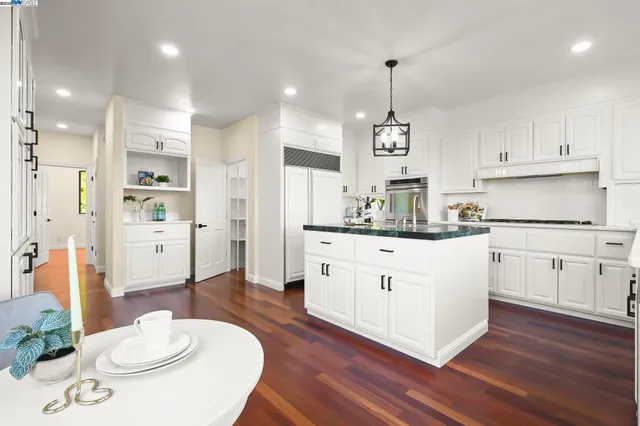 a kitchen with stainless steel appliances kitchen island granite countertop a refrigerator a white stove and white cabinets with wooden floor