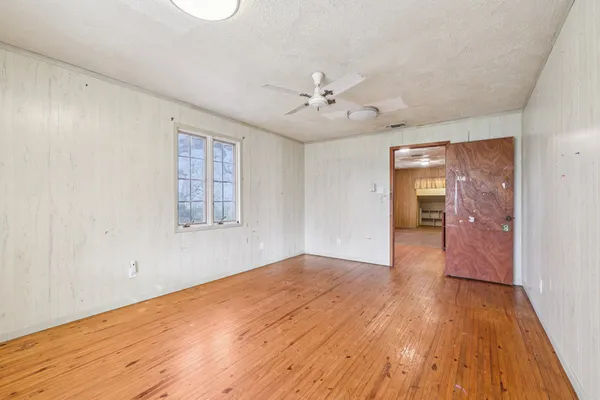 an empty room with wooden floor fan and windows
