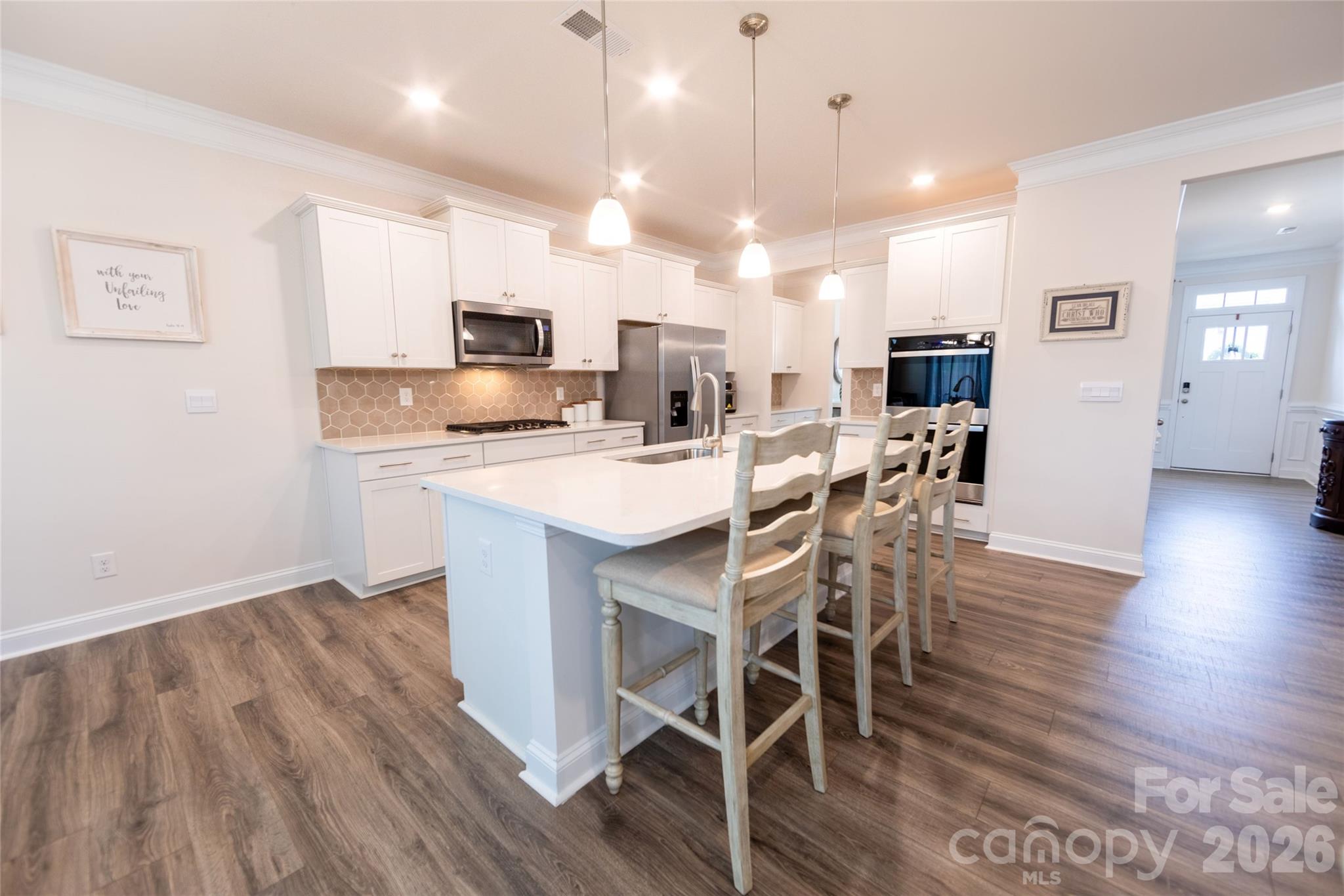 151 Aviendha Lane Troutman, NC 28166 - Photo 10 of 43 a kitchen with stainless steel appliances kitchen island granite countertop a wooden table chairs and wooden floor