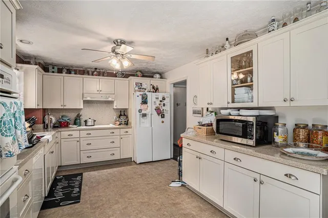 a kitchen with granite countertop a refrigerator oven a sink dishwasher and white cabinets with wooden floor