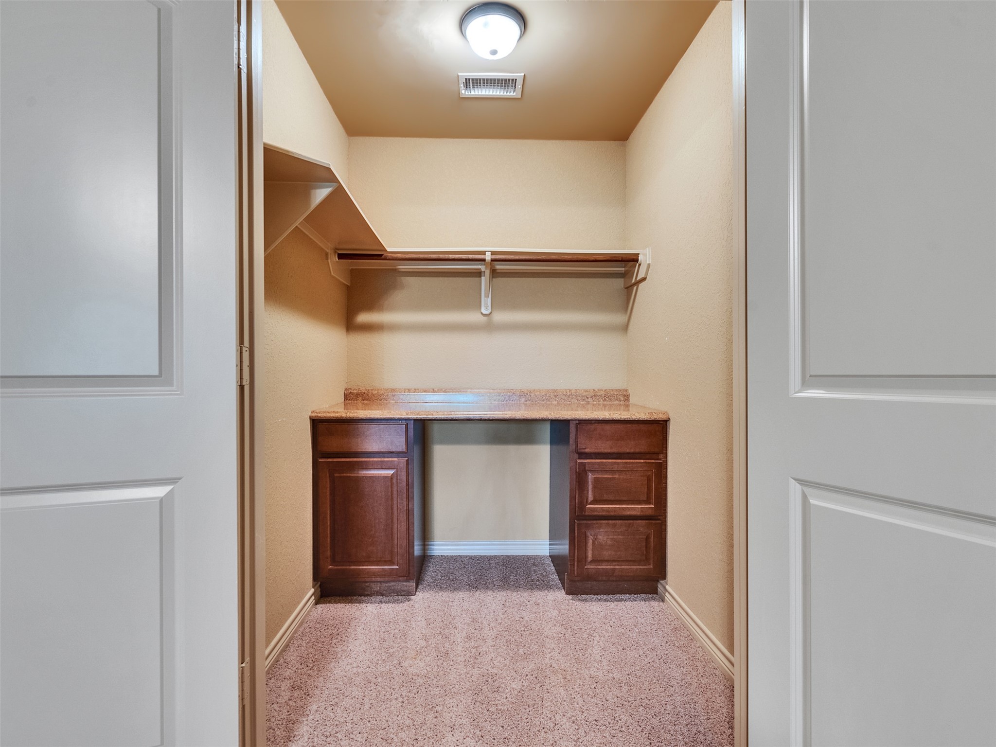 18005 Cindy Lane Conroe, TX 77302 - Photo 37 of 49 This photo features a spacious walk-in closet with a built-in wooden desk and drawers, a shelf for hanging clothes, and carpeted flooring. It's well-lit with a ceiling light, providing ample storage and workspace.