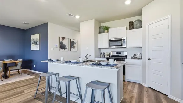 a kitchen with stainless steel appliances granite countertop a stove top oven a sink dishwasher a refrigerator and a dining table with wooden floor