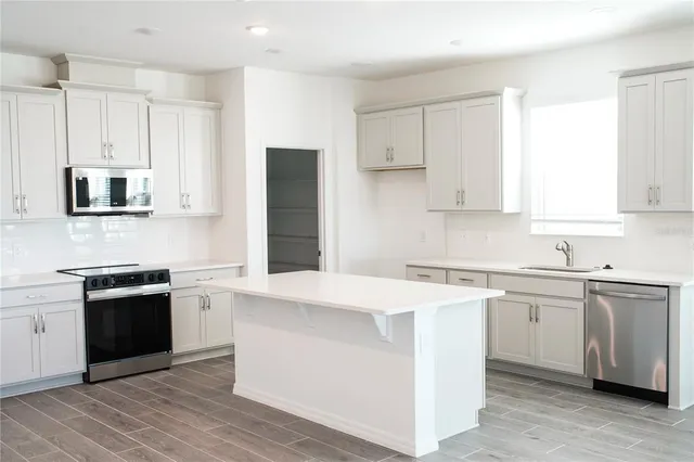 a kitchen with stainless steel appliances granite countertop a stove top oven a sink a refrigerator and white cabinets with wooden floor