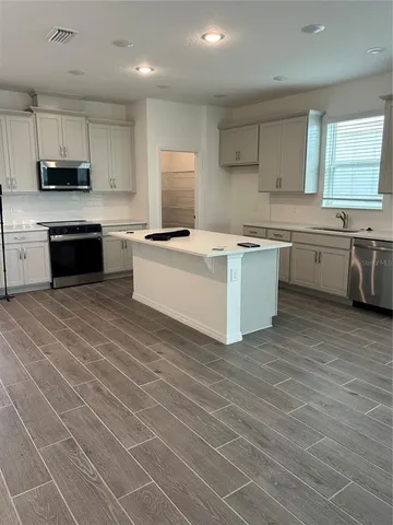 a large kitchen with stainless steel appliances a stove a sink dishwasher a refrigerator and white cabinets with wooden floor