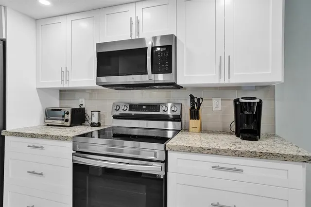 a kitchen with stainless steel appliances granite countertop white cabinets and a stove a oven with white countertops