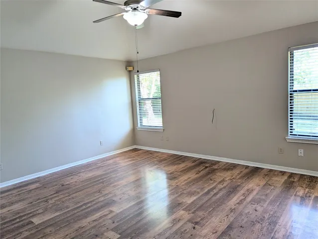 an empty room with wooden floor fan and windows