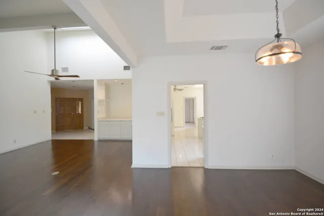 an empty room with wooden floor chandelier and windows