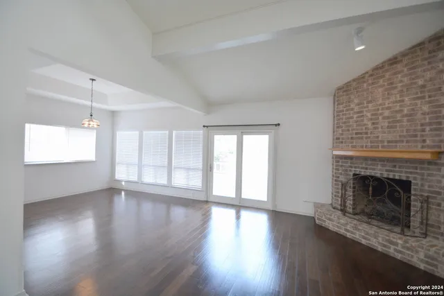 an empty room with wooden floor fireplace and windows