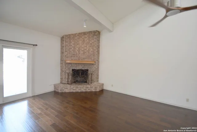a view of an empty room with wooden floor fireplace and a window