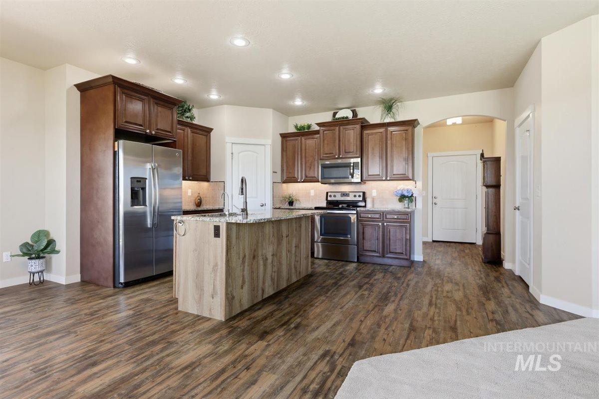 13496 Hockberger Ranch Road Caldwell, ID 83607 - Photo 15 of 40 Spacious kitchen featuring wood-finish flooring, dark wood cabinetry, a center island with a sink, stainless steel appliances, and recessed lighting