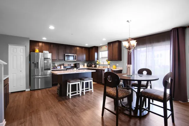 a kitchen with stainless steel appliances granite countertop a refrigerator a microwave a stove and a dining table with wooden floor