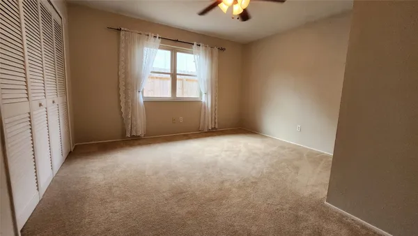 an empty room with chandelier fan and windows