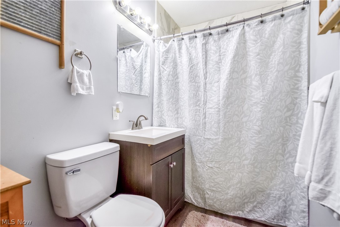 1969 Paisley Road Madison, OH 44057 - Photo 13 of 20 Bathroom featuring a white toilet, dark wood-finish vanity with a white sink, brushed nickel faucet, and a wall-mounted mirror with overhead lighting