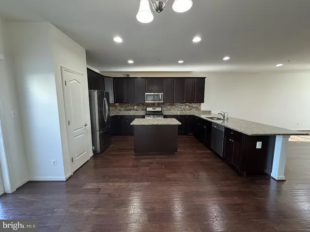 a kitchen with stainless steel appliances granite countertop a refrigerator a sink dishwasher and a microwave with wooden floor