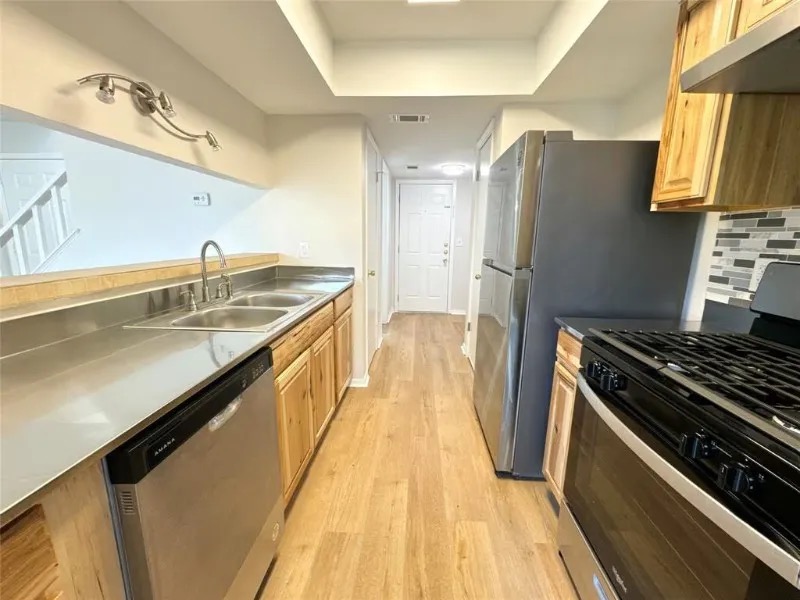 12136 Thompkins Drive, Unit B Austin, TX 78753 - Photo 3 of 7 Kitchen with stainless steel appliances, light wood-style flooring, under cabinet range hood, a tray ceiling, and tasteful backsplash