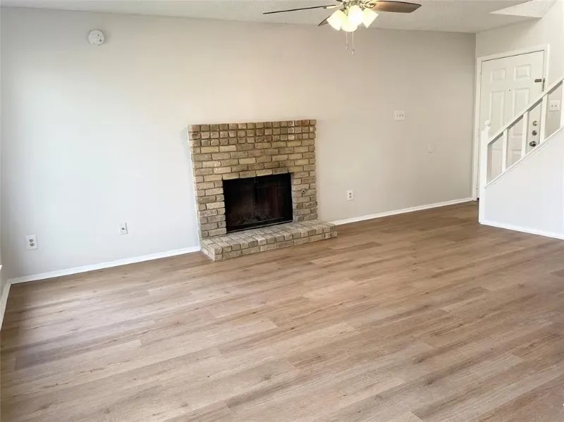 12136 Thompkins Drive, Unit B Austin, TX 78753 - Photo 4 of 7 Unfurnished living room with a ceiling fan, a brick fireplace, wood finished floors, and stairs