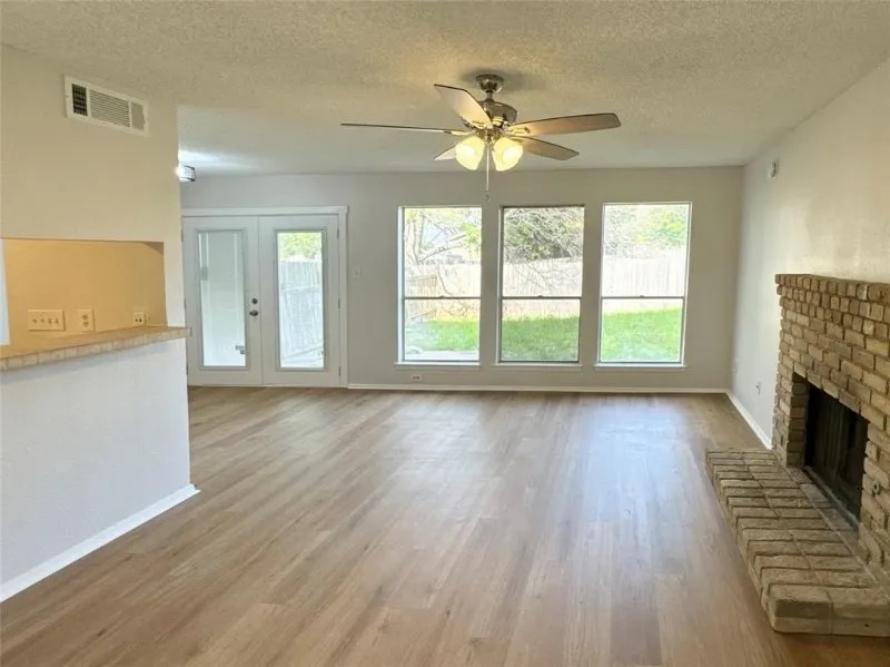 12136 Thompkins Drive, Unit B Austin, TX 78753 - Photo 5 of 7 Unfurnished living room featuring light wood-type flooring, a textured ceiling, a fireplace, healthy amount of natural light, and ceiling fan