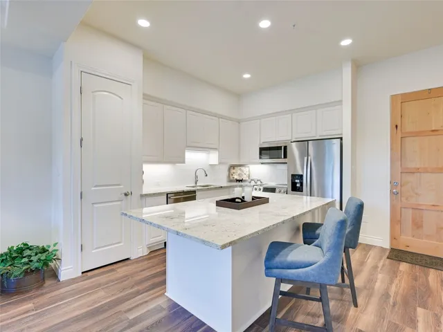 a kitchen with stainless steel appliances a refrigerator a stove a sink and white cabinets with wooden floor