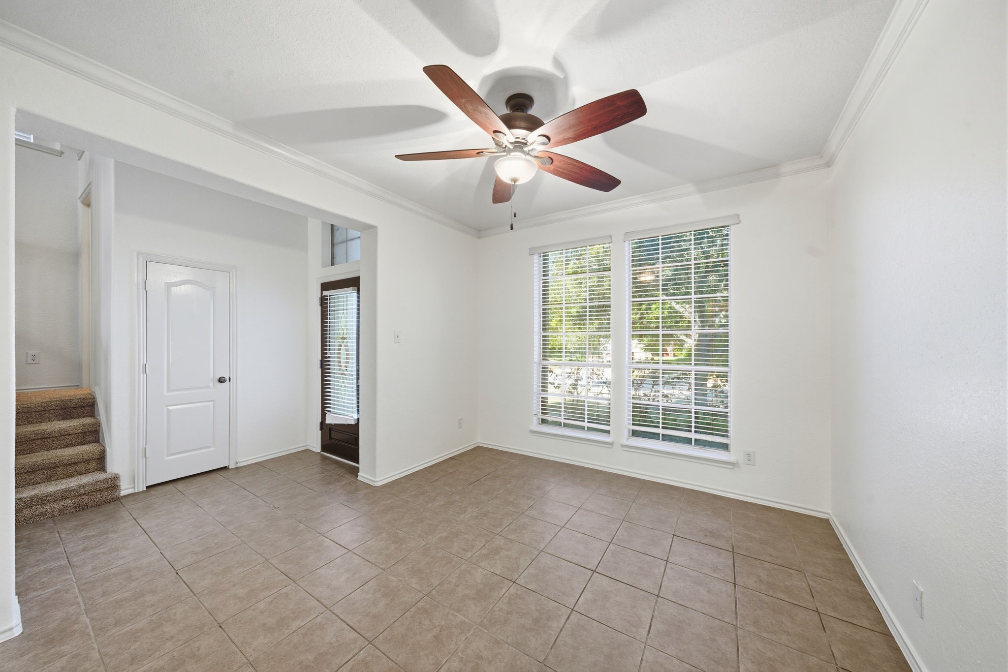 23139 Tranquil Spring Lane Katy, TX 77494 - Photo 10 of 22 Bright room with tiled flooring and large windows providing natural light. Features a ceiling fan, neutral walls, and access to a stairway and doorways.