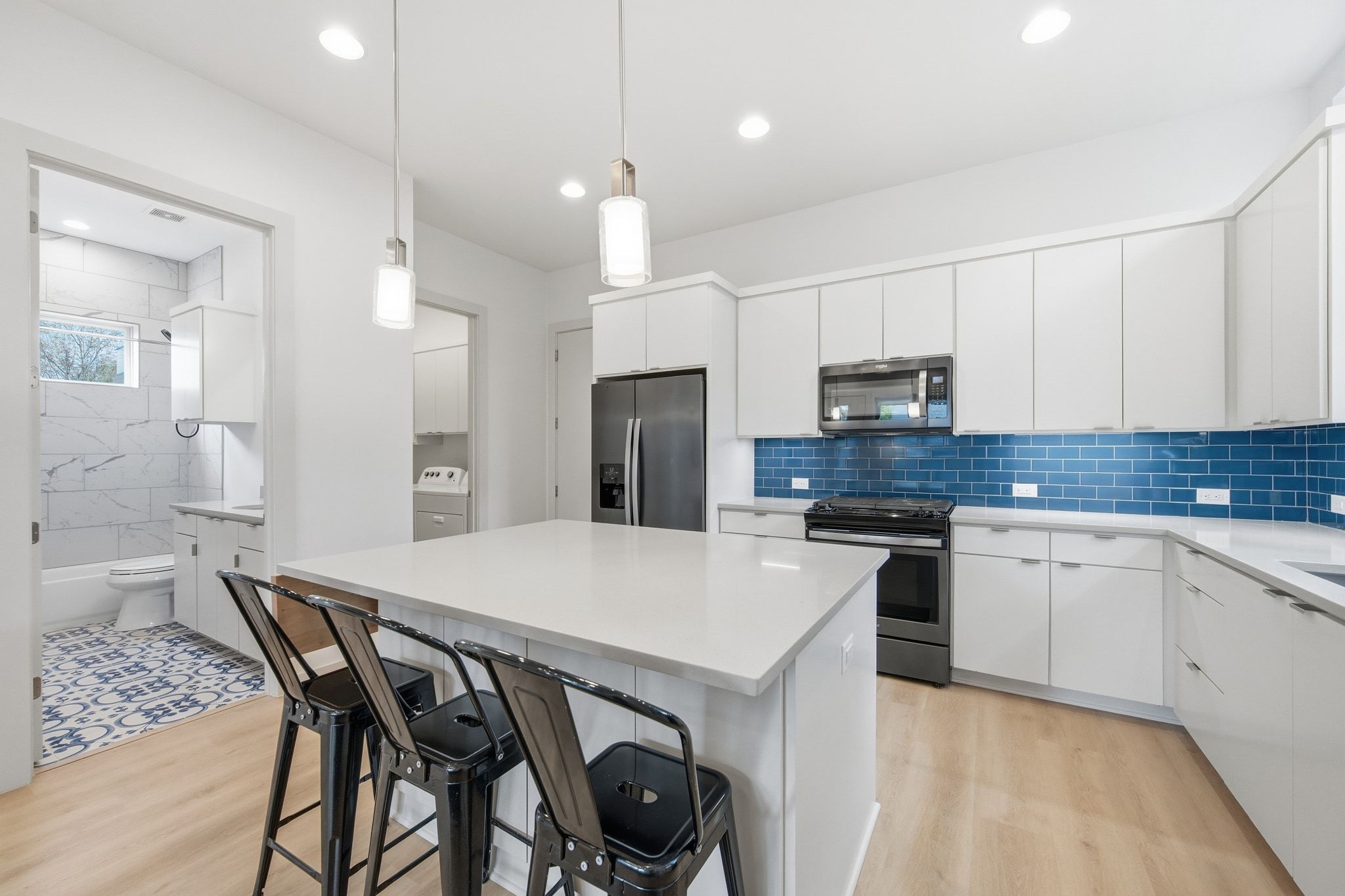 2811 Garwood Street, Unit B Austin, TX 78702 - Photo 12 of 24 Kitchen with a kitchen breakfast bar, appliances with stainless steel finishes, light wood-style flooring, white cabinets, and a center island