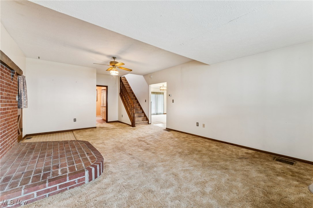 Empty room with carpet, stairway, and a ceiling fan