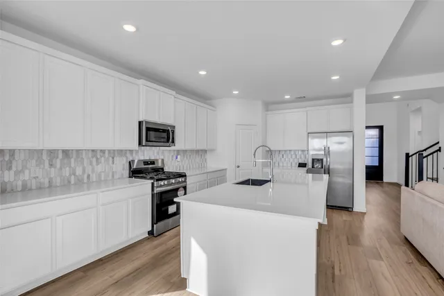 a kitchen with stainless steel appliances kitchen island granite countertop a stove top oven a sink a refrigerator and white cabinets with wooden floor