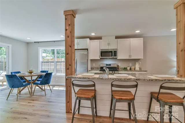 a kitchen with stainless steel appliances granite countertop a stove a sink a microwave a dining table and chairs with wooden floor