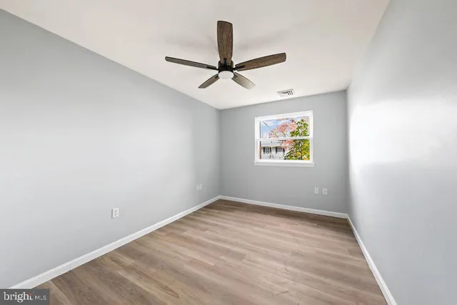 an empty room with wooden floor ceiling fan and window