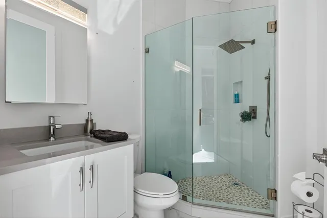 a bathroom with a granite countertop sink a mirror a toilet and shower