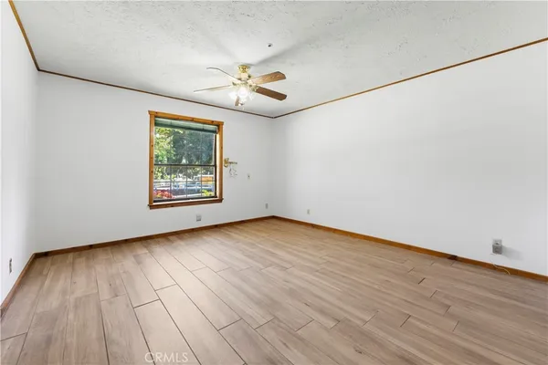 an empty room with wooden floor chandelier fan and windows