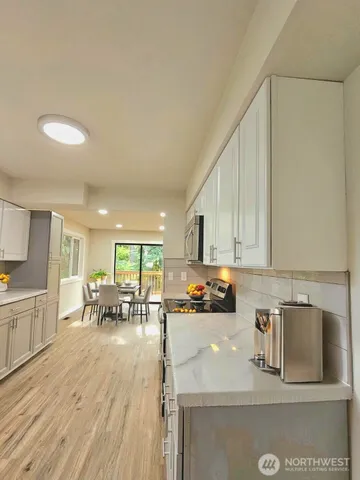 a kitchen with stainless steel appliances granite countertop a stove a sink a refrigerator and white cabinets with wooden floor