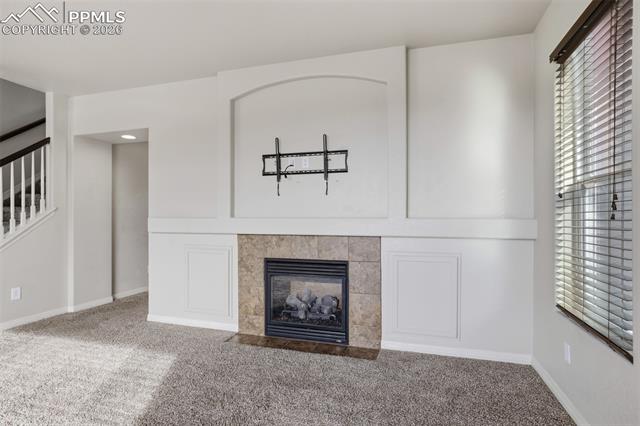 2224 Reed Grass Way Colorado Springs, CO 80915 - Photo 13 of 39 Unfurnished living room featuring a fireplace, carpet, and stairway