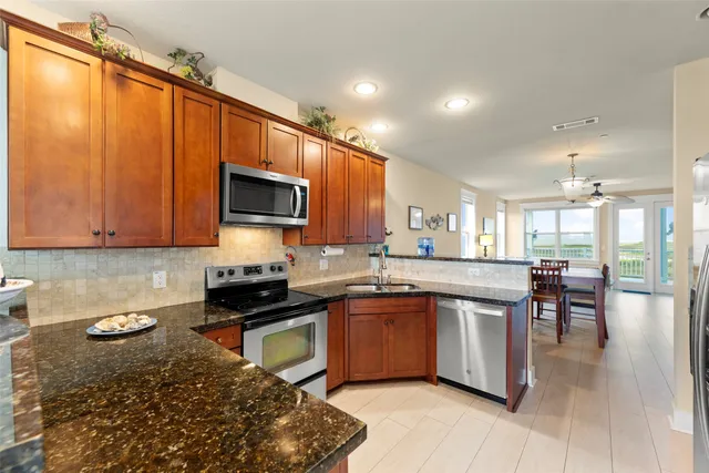 a kitchen with stainless steel appliances granite countertop a stove top oven a sink dishwasher a dining table and chairs with wooden floor