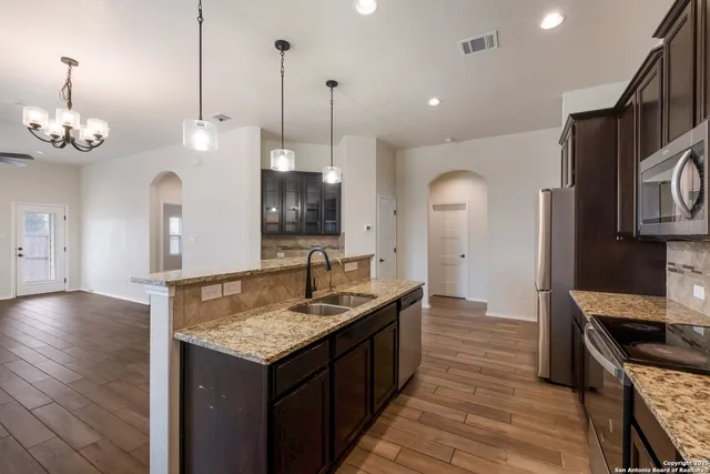 a kitchen with kitchen island granite countertop a stove a sink a center island and wooden floor