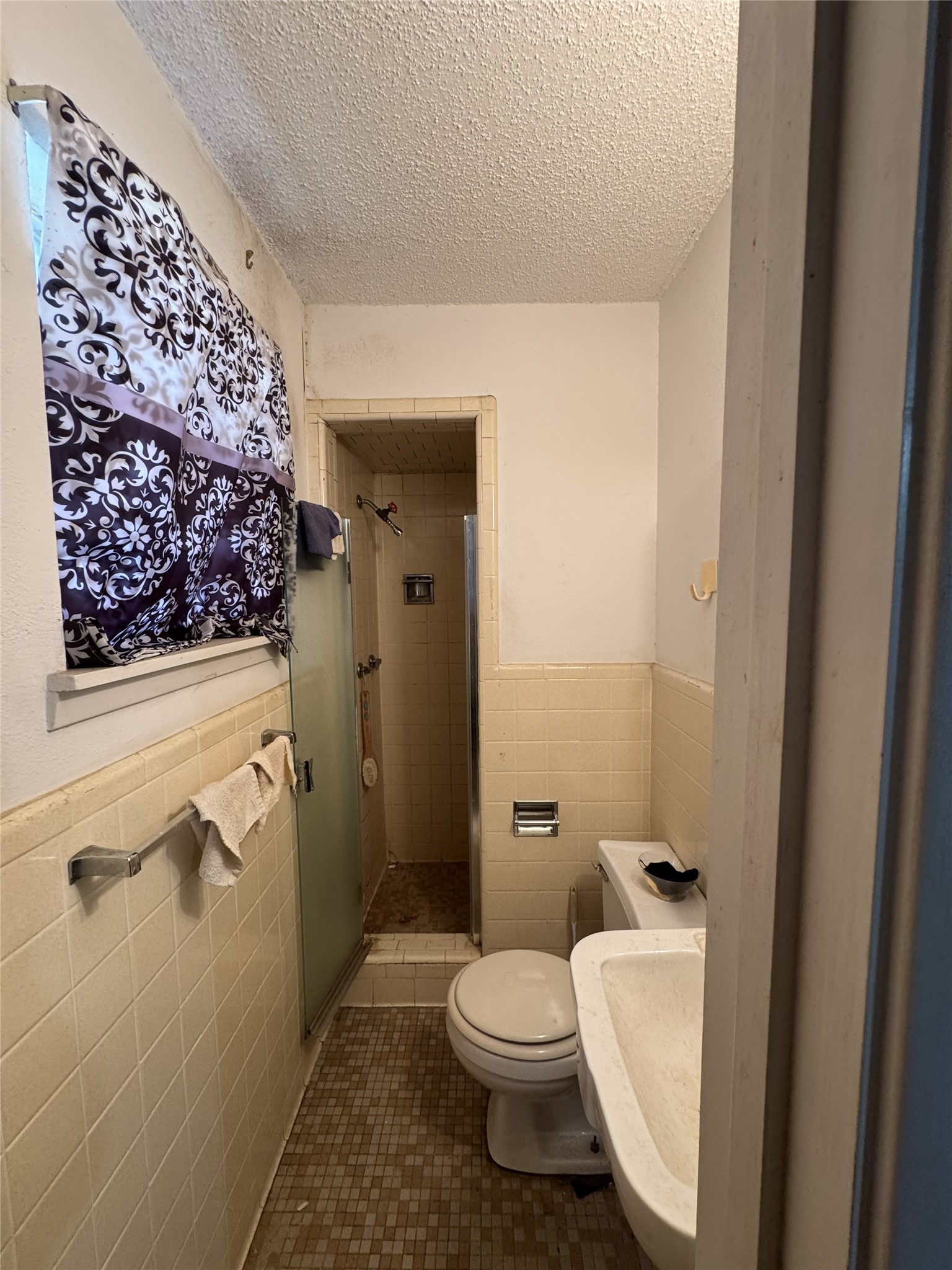 106 North 7th Street Dawson, TX 76639 - Photo 15 of 28 Bathroom featuring tile walls, a wainscoted wall, a textured ceiling, a stall shower, and dark tile patterned floors
