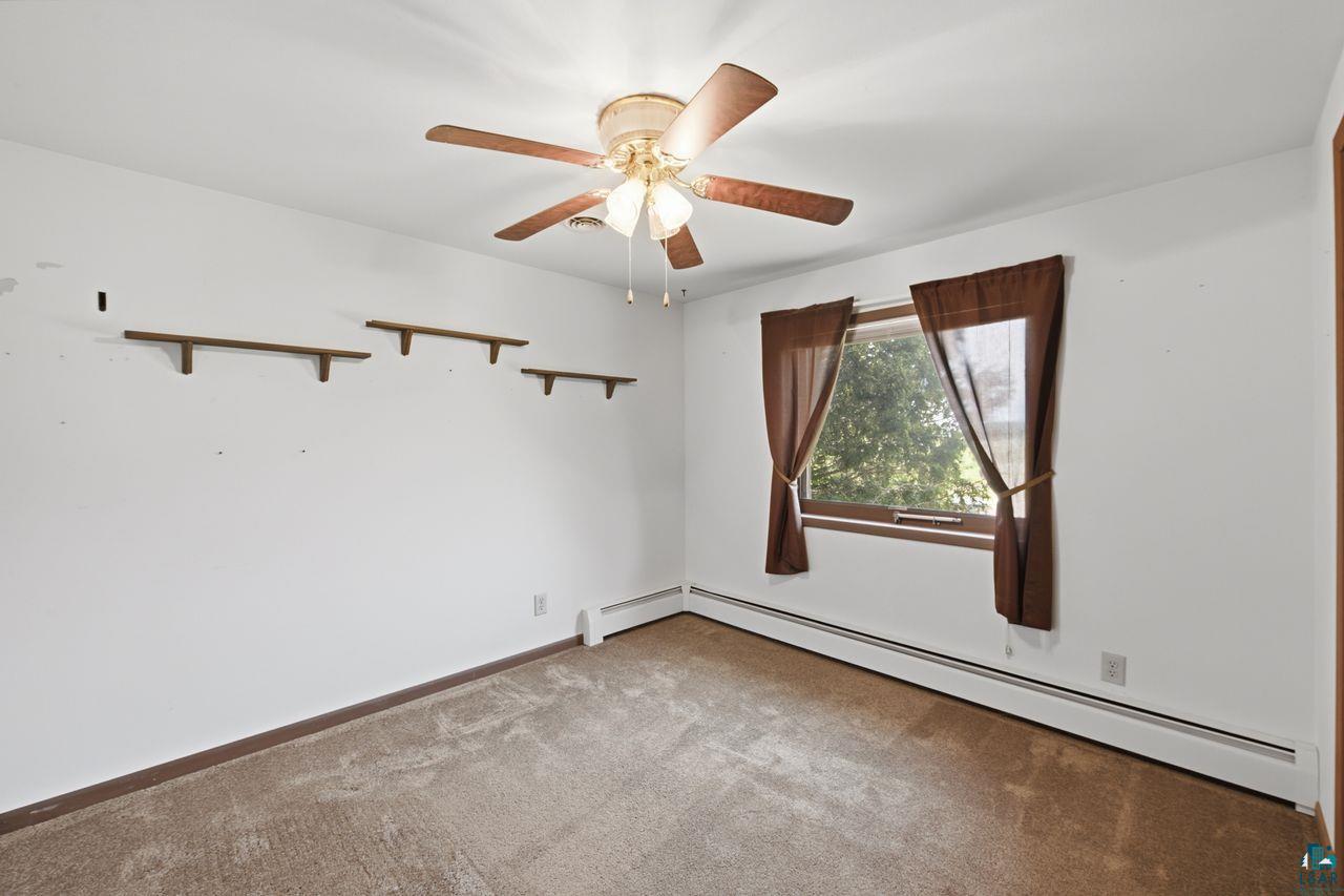 61018 Dahlstrom Road Ashland, WI 54806 - Photo 2 of 28 Room featuring a ceiling fan with light, wall-mounted shelving, a window with exterior greenery, and baseboard heating