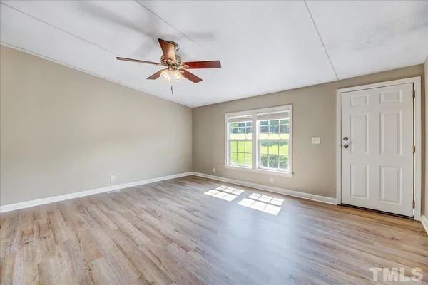 an empty room with wooden floor fan and windows