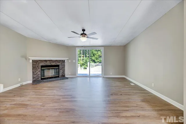 a view of an empty room with wooden floor fireplace and a window
