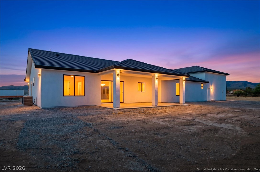 5910 East Kellogg Road Pahrump, NV 89061 - Photo 43 of 58 A striking modern dwelling bathed in the warm glow of evening lights, set against a vibrant twilight sky.