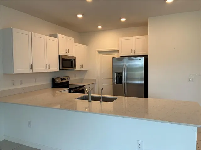 a kitchen with a refrigerator a microwave a stove and white cabinets with wooden floor