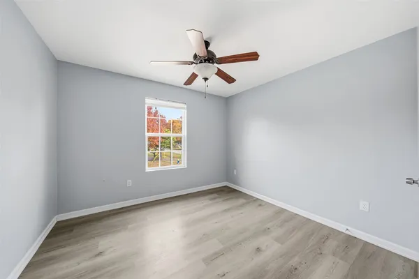 an empty room with wooden floor ceiling fan and windows