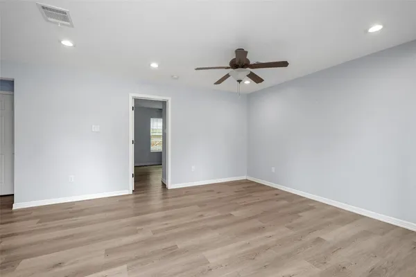 a view of an empty room with wooden floor and ceiling fan