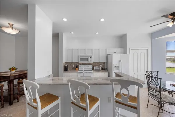 a kitchen with stainless steel appliances kitchen island granite countertop a dining table chairs and a refrigerator