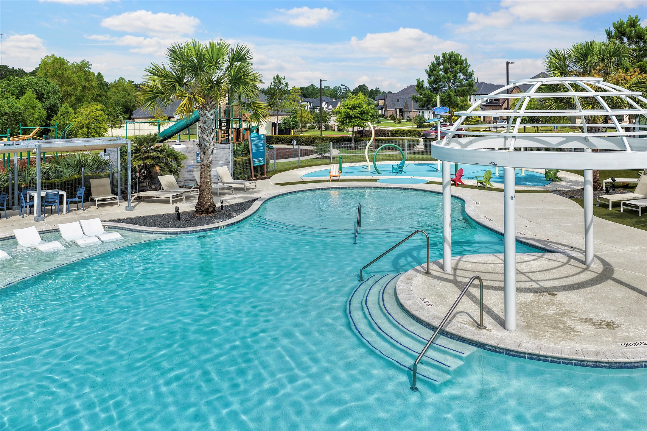 10603 Whitejacket Conroe, TX 77385 - Photo 39 of 42 This photo showcases a beautifully designed community pool area featuring a large swimming pool with in-water loungers, a shaded seating area, a playground with a slide, and lush landscaping. Ideal for family relaxation and outdoor enjoyment.