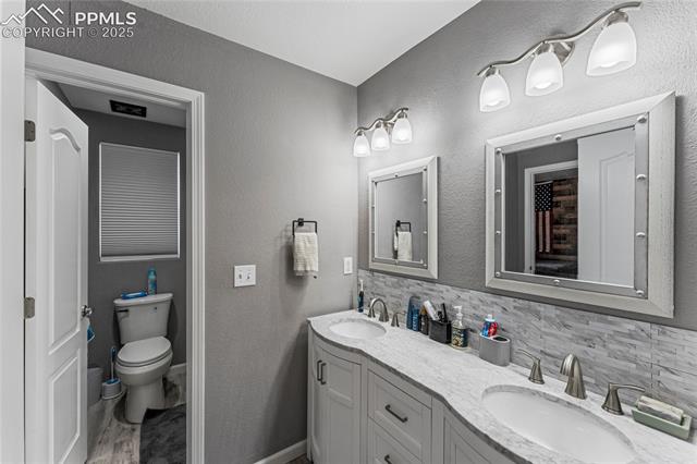 10158 Angeles Road Peyton, CO 80831 - Photo 23 of 43 Bathroom featuring a sink, tasteful backsplash, double vanity, and toilet